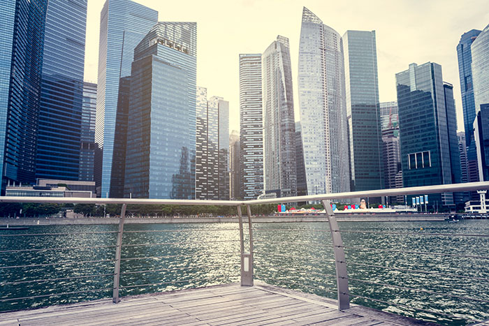City waterfront with modern skyscrapers reflecting on water under a cloudy sky at sunset.