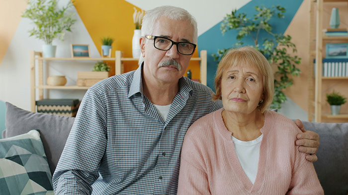 Elderly couple sitting on a sofa looking concerned, reflecting on family issues involving woman accused of sleeping with sister&rsquo;s fianc&eacute;.