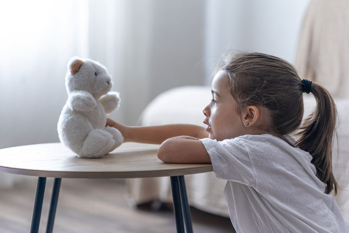 Young girl playing with a teddy bear symbolizing estranged dad leaving everything to daughter and inheritance dispute with stepmom.