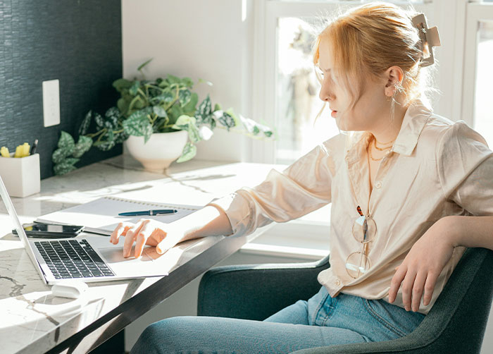 A woman sits at a desk, looking intently at a laptop, contemplating her job and marriage after disrespect.