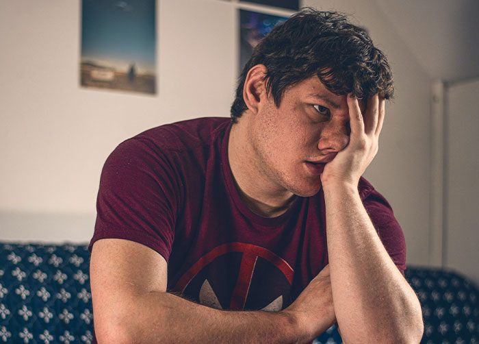 A man in a burgundy shirt rests his face in his hand, looking concerned. He may be thinking about quitting her job.
