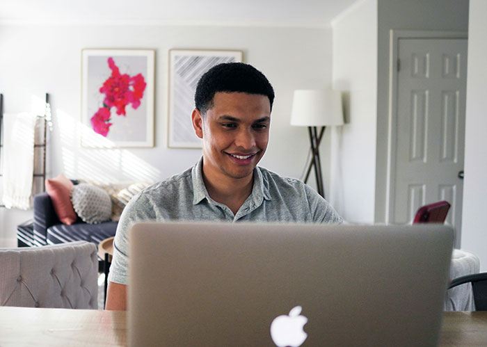 Man smiling at a laptop screen in a bright, modern living room. Reflects themes of work-life and relationship choices like quitting her job.