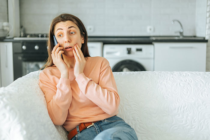 Woman uses Shazam on phone looking surprised while sitting on couch in modern kitchen setting. Woman uses Shazam on phone looking surprised while sitting on couch in modern kitchen setting.