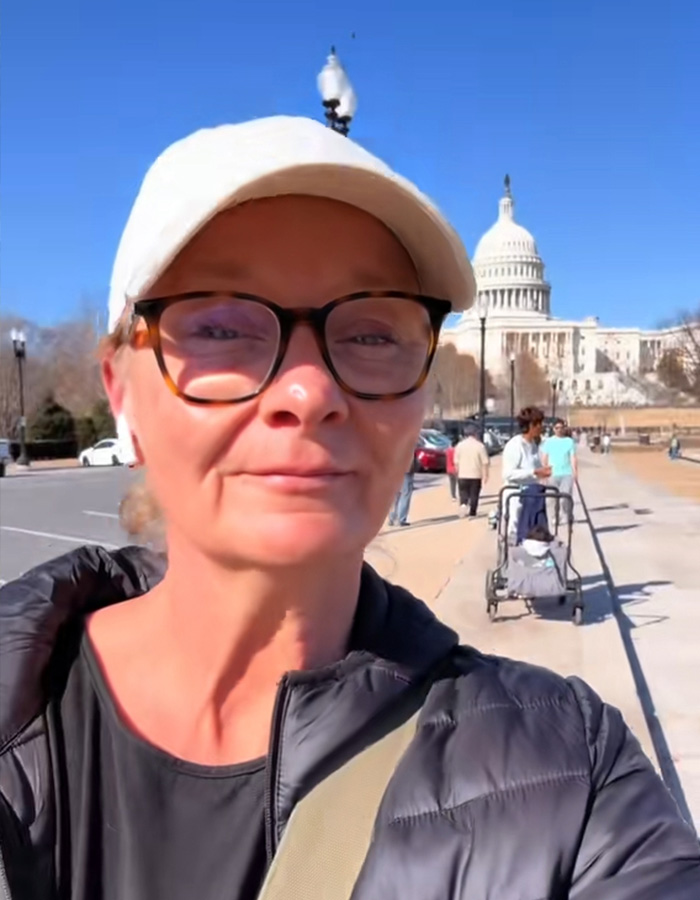 Woman in a white cap and glasses taking a selfie with the US Capitol in the background. **DC Woman's Back Alley Figure.**