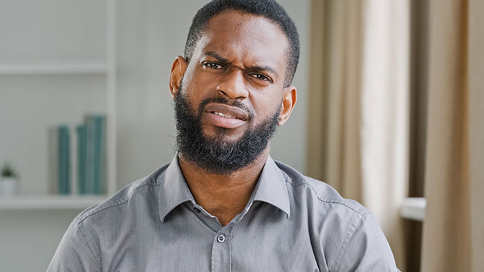 A man with a beard and gray shirt makes a disgusted face. He represents the mean, inconsiderate, and dumb boyfriends and husbands in online vents.