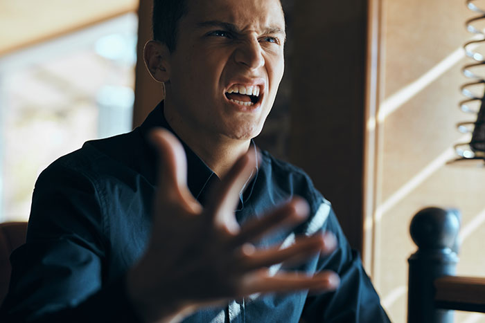 An angry, frustrated man in a dark shirt, yelling and gesturing. Boyfriends and husbands acting mean.