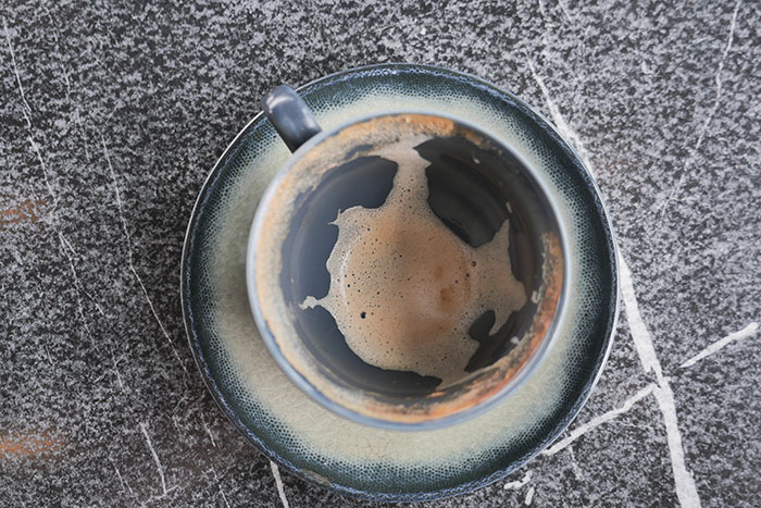 An empty coffee cup with foam residue, on a matching saucer, against a dark marble surface. Boyfriends and husbands.