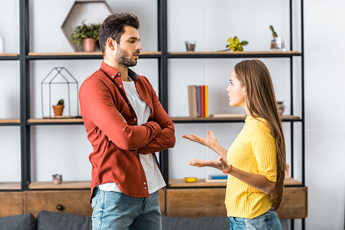 A man with crossed arms looks annoyed while a woman gestures, discussing how boyfriends and husbands can be mean.