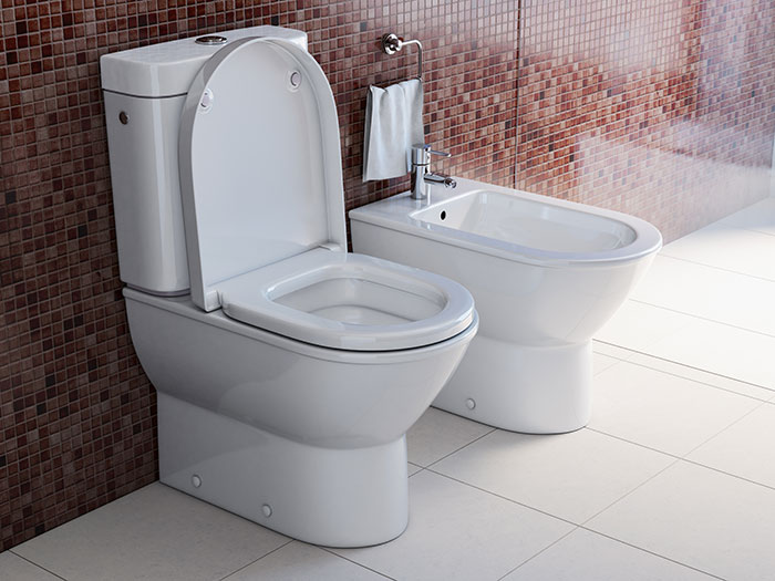 A modern white toilet with the seat up next to a bidet in a tiled bathroom, depicting mean, inconsiderate, and dumb behavior.