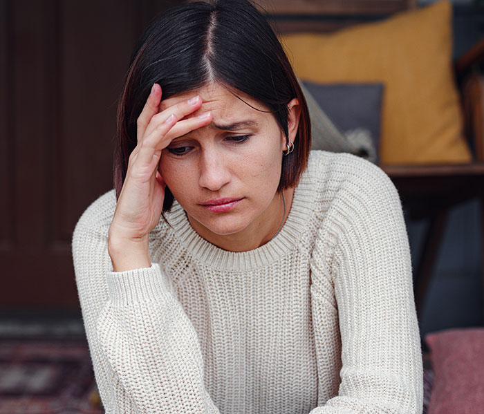 A woman looking distressed, holding her forehead, feeling the pain of boyfriends and husbands being mean.