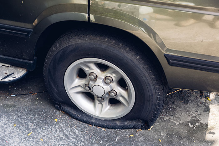 A flat tire on an olive green car, symbolizing a mean, inconsiderate, or dumb boyfriend or husband moment.