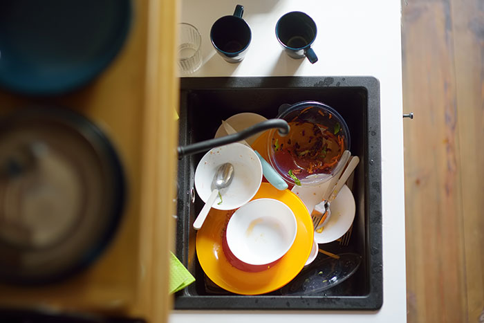 A kitchen sink overflowing with dirty dishes and food scraps, illustrating the inconsiderate behavior of boyfriends and husbands.