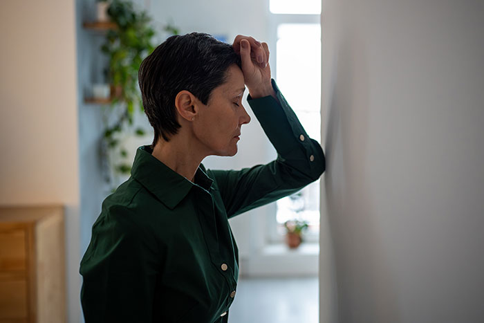 A woman in a dark green shirt leaning against a wall, looking distressed. She is likely dealing with mean boyfriends or husbands.