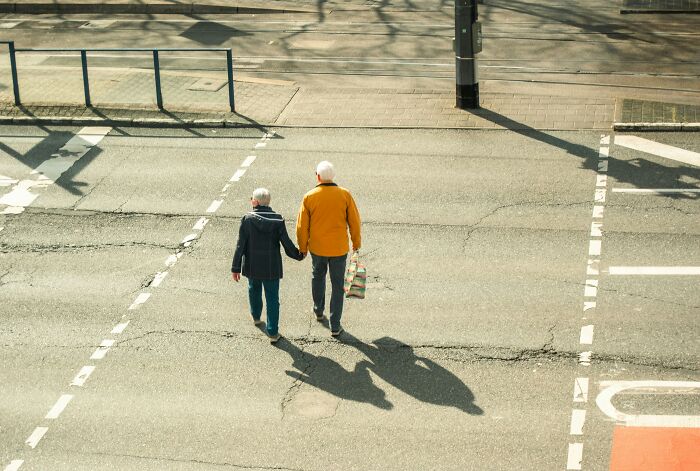 Elderly couple walking hand in hand across an urban street, illustrating trusted urban legends unexpectedly true.
