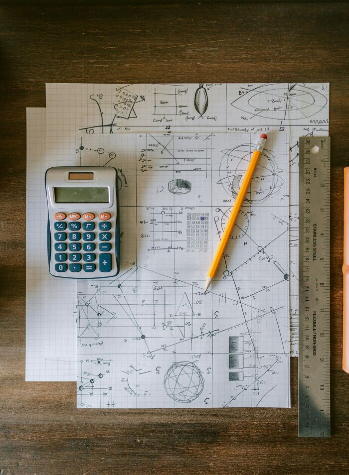 Calculator, pencil, and ruler on papers with complex geometric drawings demonstrating intelligence and problem solving skills.