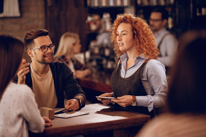 A waitress delivering silent satisfaction while taking orders from customers in a busy restaurant setting.