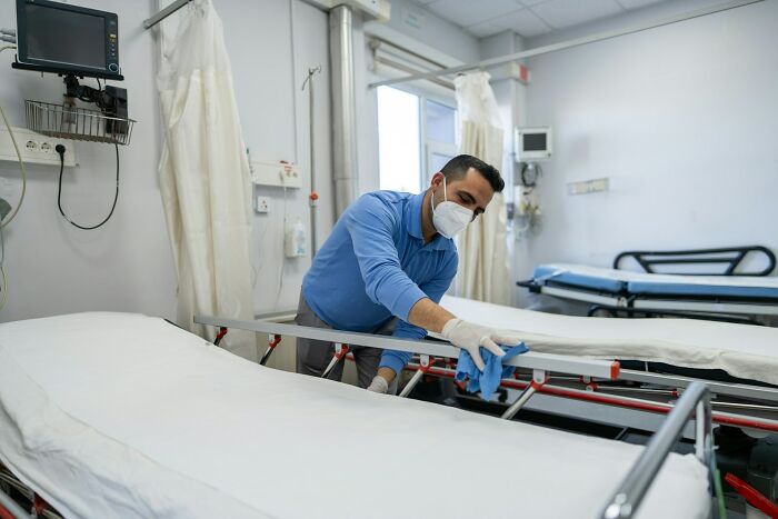 Hospital worker wearing mask cleaning a hospital bed in a ward highlighting hidden truths about hospitals and patient care safety.