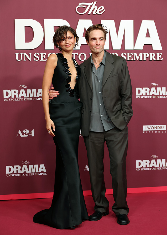 Zendaya wearing a sheer black dress with a plunging neckline, posing with a man in a suit at a movie promo event.