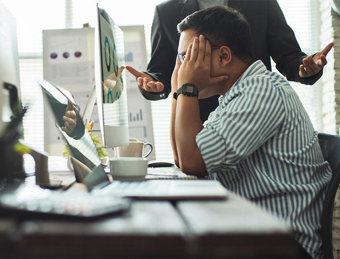 Developer A looks stressed as a colleague gestures aggressively at a computer. A "budget burden" scenario often leads to this.