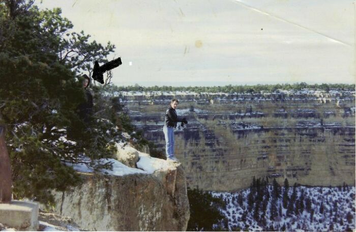 Mysterious figure hidden in tree near cliff with people overlooking canyon landscape