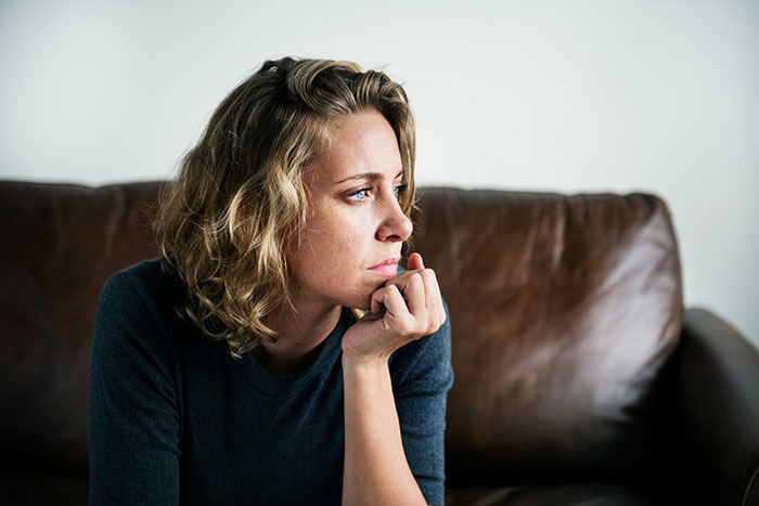 A pensive woman with blonde hair, resting her chin on her hand, contemplating MIL's darkest secret.