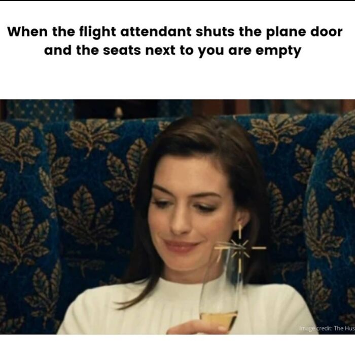 A woman subtly smiles, holding a drink on a plane, portraying the joy of empty adjacent seats. Travel memes for your desk.