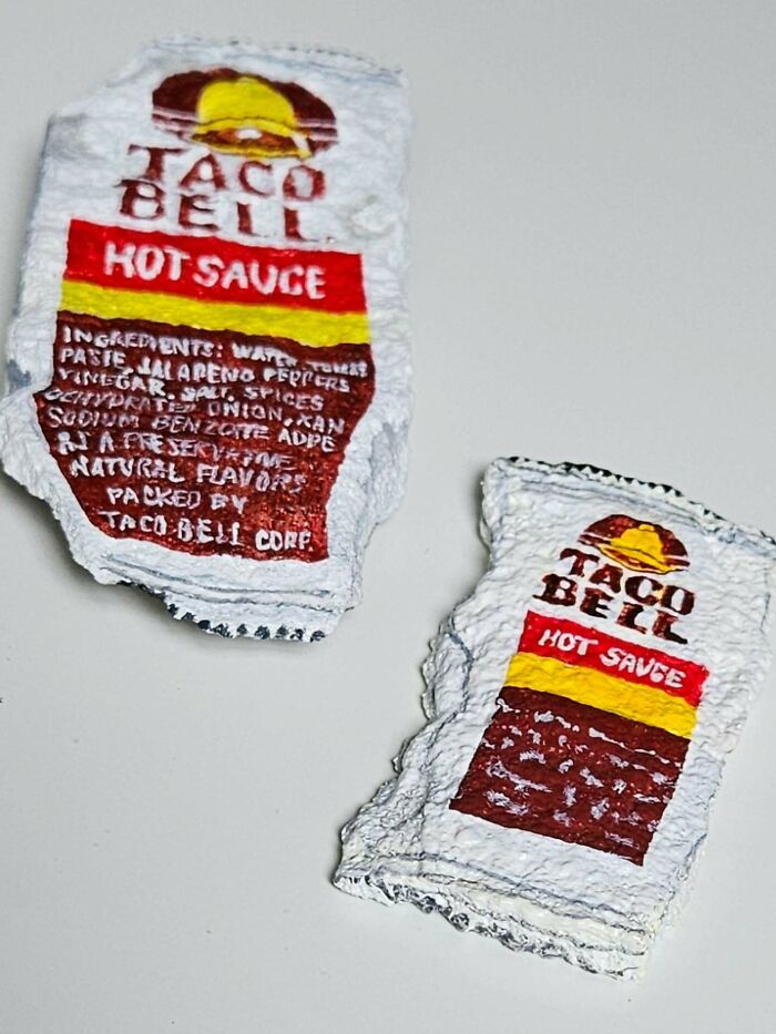 Two colorful stone creations sculpted as Taco Bell hot sauce packets, one larger, displaying ingredients, turning rocks into iconic foods.