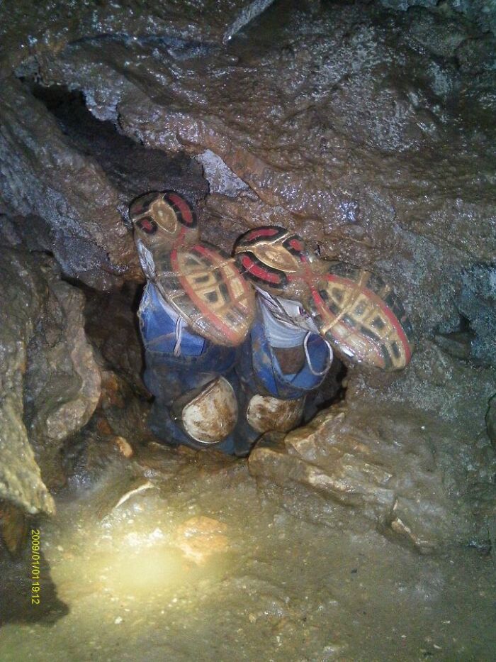 A person's legs, clad in dirty blue overalls and boots with red and black soles, stuck in a tight cave passage. Disturbing d***h stories.