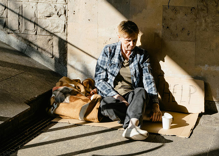 A person, possibly homeless, sits with a blanket and a HELP sign, highlighting challenges people of low intelligence might face.