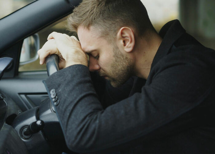 Man in car, head on steering wheel, worried about the economy and his wallet. Stress over financial instability.