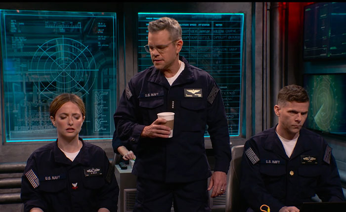 Matt Damon in a US Navy uniform, holding a coffee cup, surrounded by two others, in a SNL sketch.