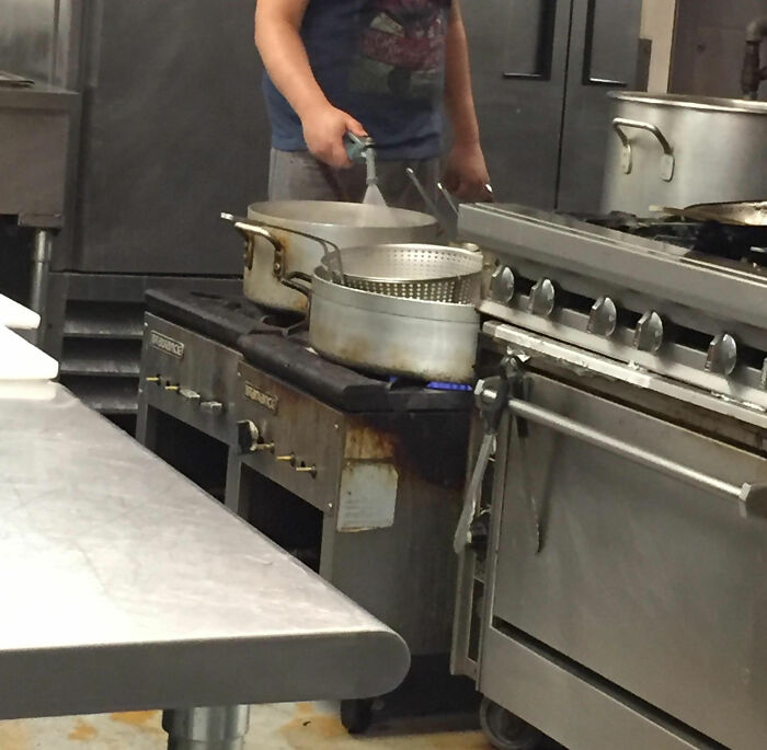 Restaurant worker cooking with pots on a greasy stove