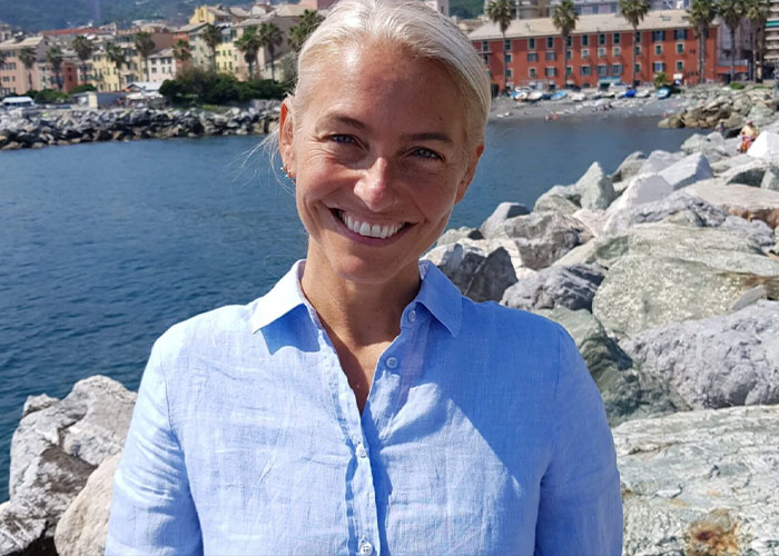 Smiling woman standing near rocky waterfront under blue sky
