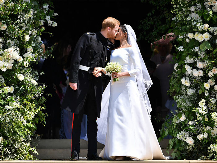 Meghan Markle and Prince Harry kissing outside church on their wedding day with floral arch