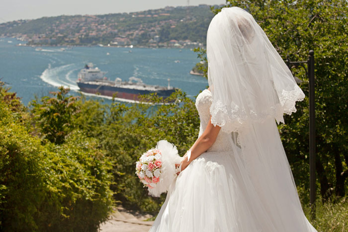 Bride in wedding dress overlooking water sailing boat background