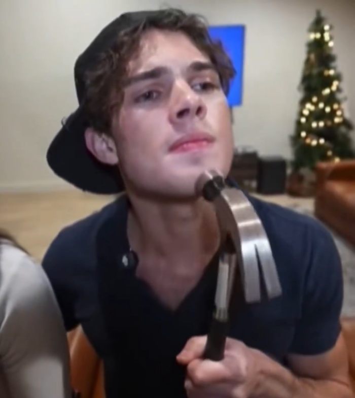 Young man holding hammer near face with looksmaxxing concern