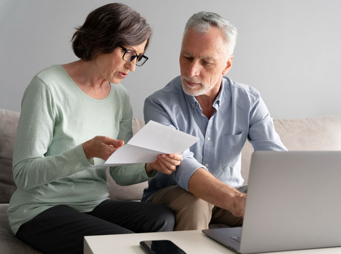 Mature couple reviewing papers and using laptop discussing inheritance money Mature couple reviewing papers and using laptop discussing inheritance money