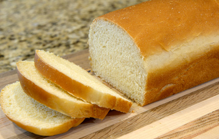 A loaf of white bread, partially sliced, on a wooden cutting board, looking like one of the weirdest packages.