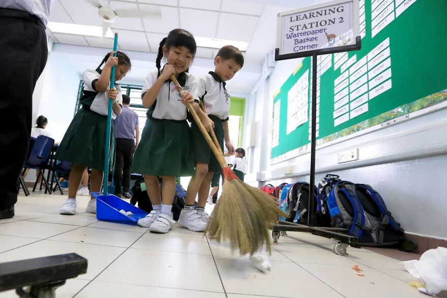 Children in uniform sweeping a classroom floor, demonstrating a common Japanese practice of shared responsibility.