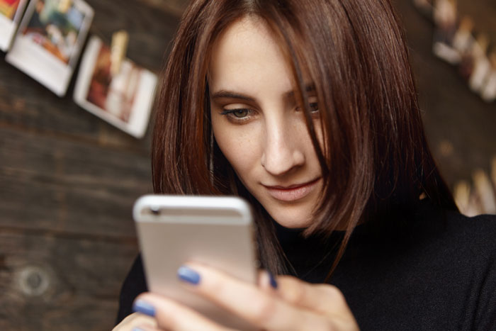 A young woman with brown hair intently looking at her phone, likely checking facts on Reddit.