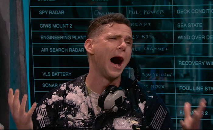 A man splattered in white goo, yelling with hands raised, near a display screen from the Matt Damon SNL sketch.