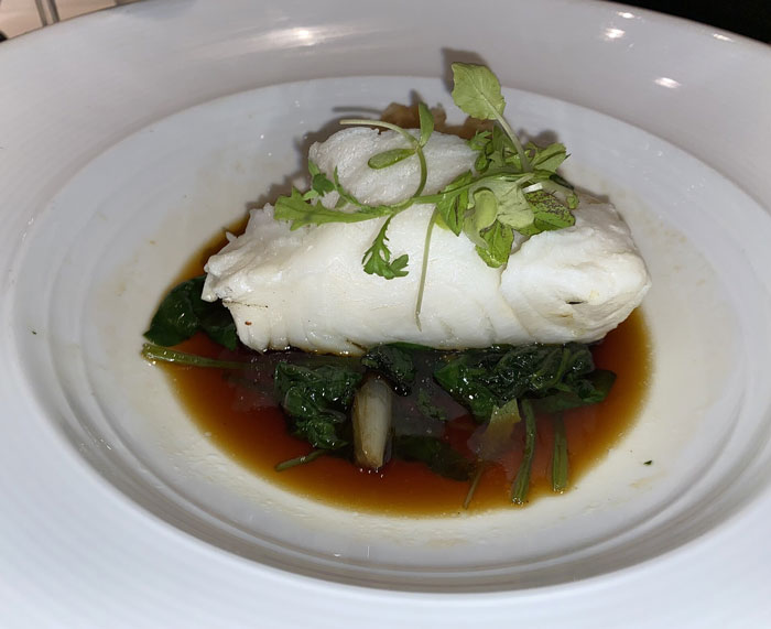 Plated artisinal white fish fillet with greens and sauce