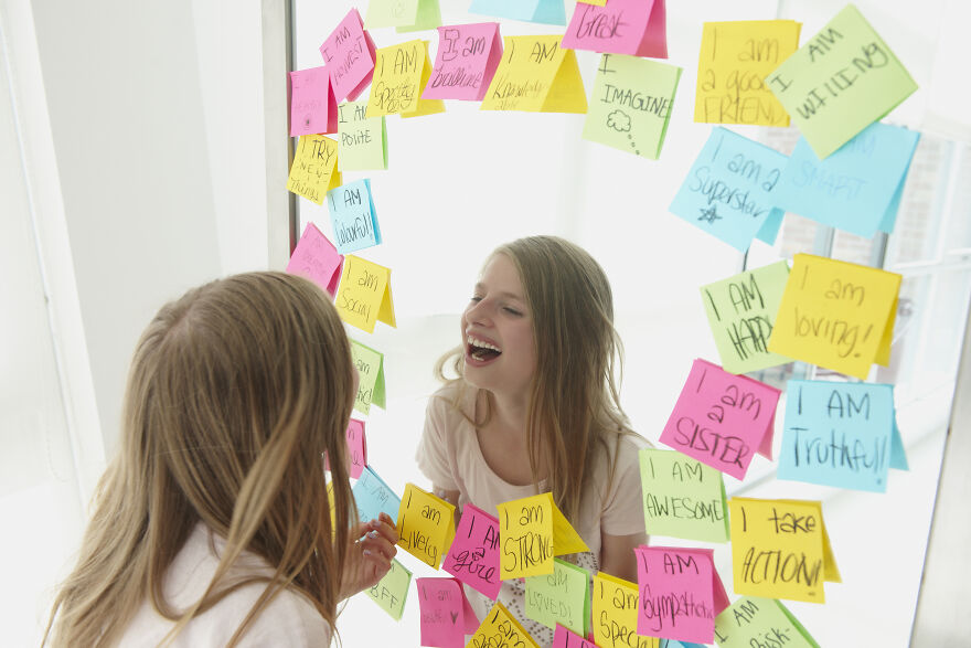 Girl smiling at mirror surrounded by positive affirmations mood booster