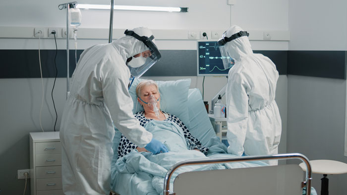 Healthcare workers in protective gear caring for patient in hospital bed