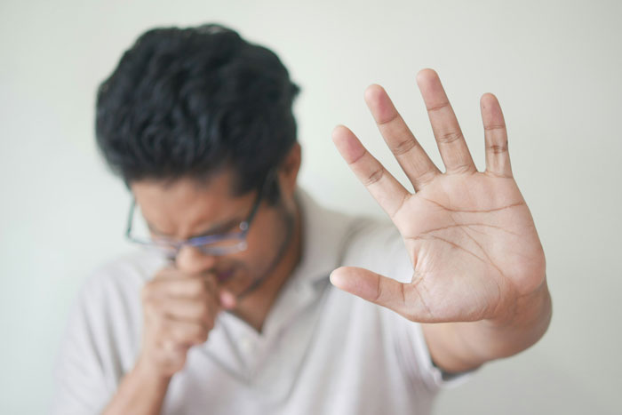 Man coughing and raising hand as a gesture to stop