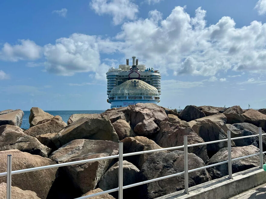 Cruise ship docked behind large rocks near small countries coastline