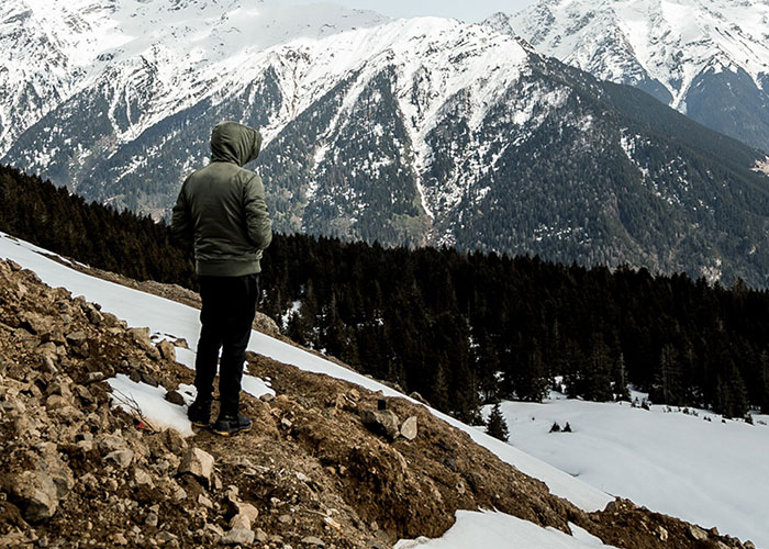 Person in hoodie standing on mountain slope with snow