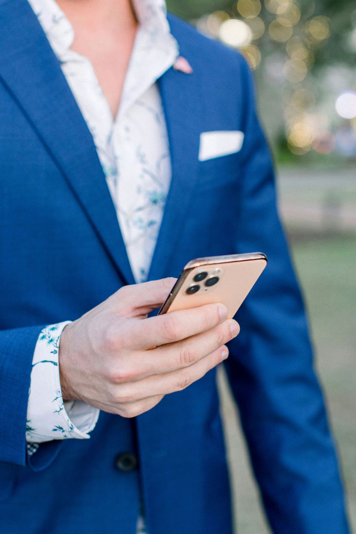Man in blue suit holding phone at wedding reception close-up