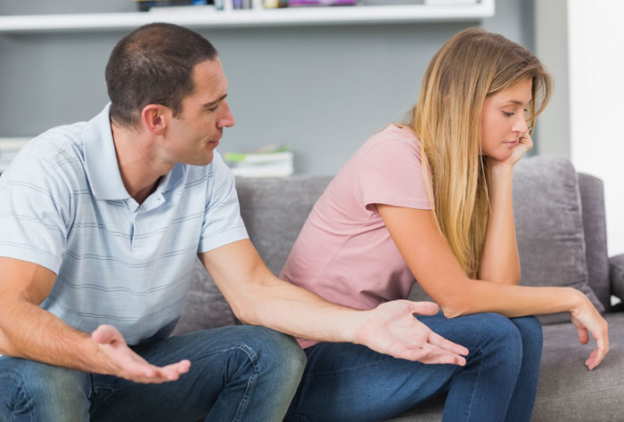 Husband and wife sitting on couch looking upset during serious discussion