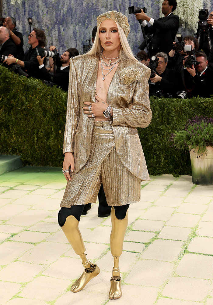 A woman in a gold suit, beret, and shiny gold prosthetic legs on a green carpet, one of the worst dressed stars at Met Gala 2026.